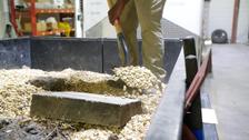 Person shoveling gravel from a trailer bed inside a warehouse with shelves in the background.