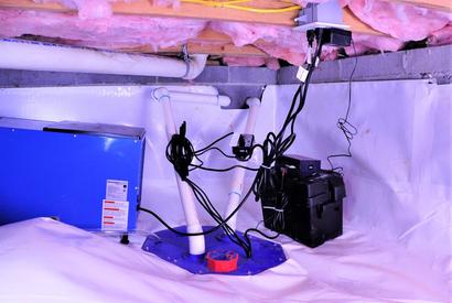 Basement sump pump system with exposed wires and pipes on a plastic-covered floor under insulation.