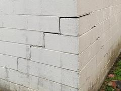 Cracked and shifted cinder block wall at the corner of a building, showing signs of structural damage.