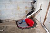 A sump pump system installed in a basement corner with exposed pipes and wiring.