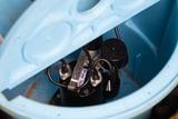 A close-up of a sump pump installed inside a blue plastic basin with wiring visible.