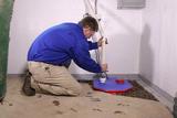 Man kneeling on floor, installing or repairing a sump pump system in a basement corner.