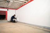 A worker installs sump pump in an unfinished basement with exposed beams.