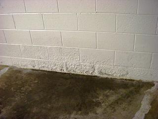 A white brick wall with visible moisture damage near the floor on a concrete surface.