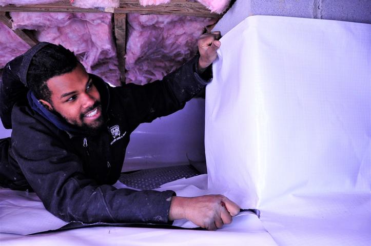 A man wraps columns in a crawl space with a vapor barrier.