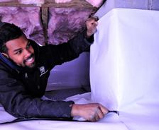 A man wraps columns in a crawl space with a vapor barrier.
