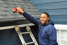 Worker on a ladder with power drill installing Aquastop Gutter Solution