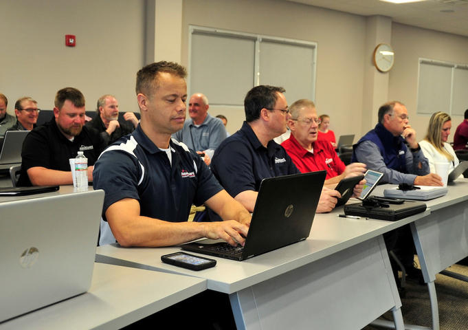 Workers sitting at tables with laptops for sales training