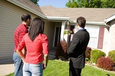 A realtor points towards the entrance, highlighting recent foundation repairs as the couple observes from the front yard.