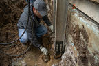 A technician installing push piers into the ground by a house's foundation