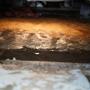 Wet, muddy ground inside a dimly lit crawl space shows clear signs of moisture, with water reflecting the light.
