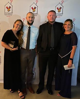 Four people dressed formally, posing in front of a Ronald McDonald House Charities backdrop.