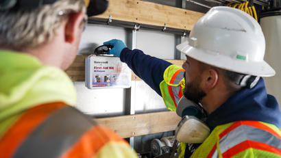 Two construction workers in safety gear accessing a first aid kit mounted on a wall.