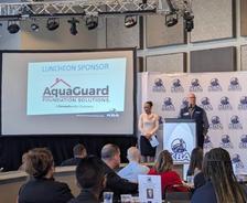 People at a business event with a presentation screen showing a sponsor's logo.