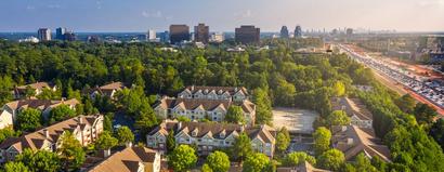 Aerial view of suburban Atlanta apartments with trees, highways, and city buildings in the distance under a clear sky.