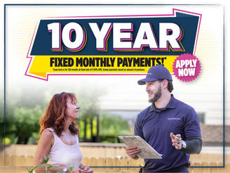A woman talks to a man in a blue uniform holding a clipboard under a sign about 10 year fixed monthly payments.