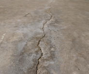 Close-up of a long crack running through a worn, concrete floor.