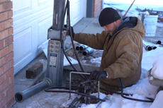 Worker in winter clothes installs a hydraulic pole near a garage on a snowy day.