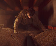 Worker crawling in a dimly lit crawl space, moving gravel with a shovel in the background.
