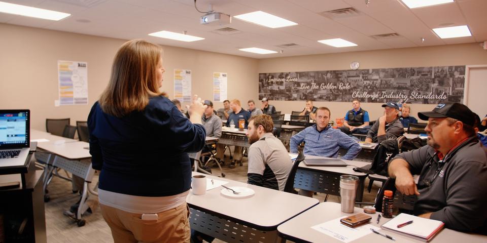 A person leading a classroom session with attentive participants seated at desks.