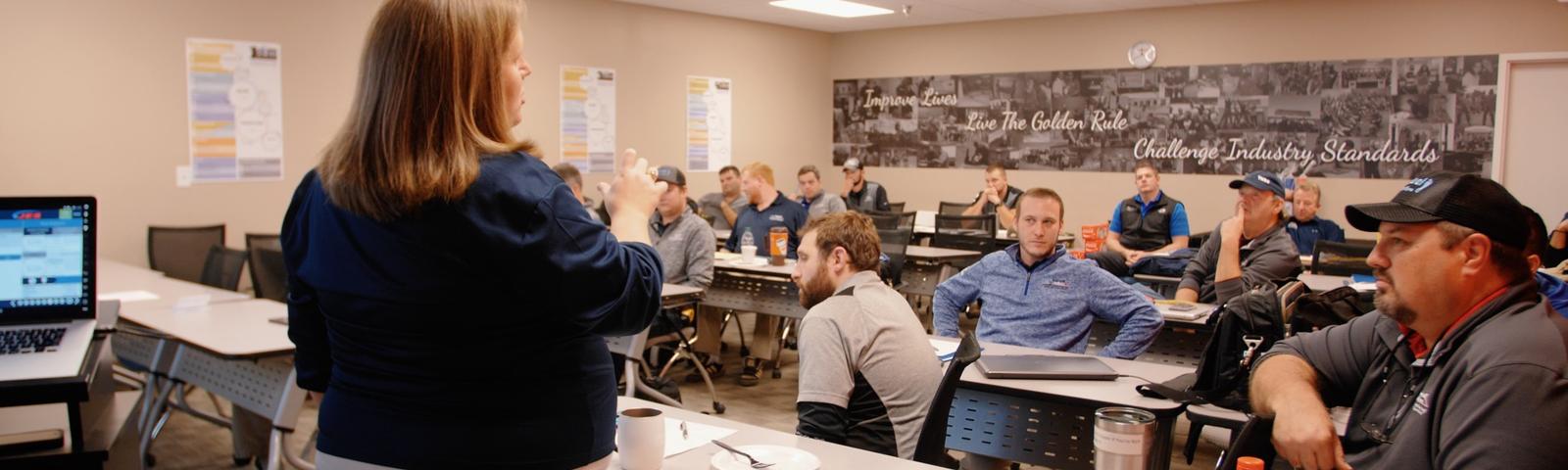 A person leading a classroom session with attentive participants seated at desks.