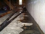A basement with water seeping through the floor and black pipes lying on the concrete surface.