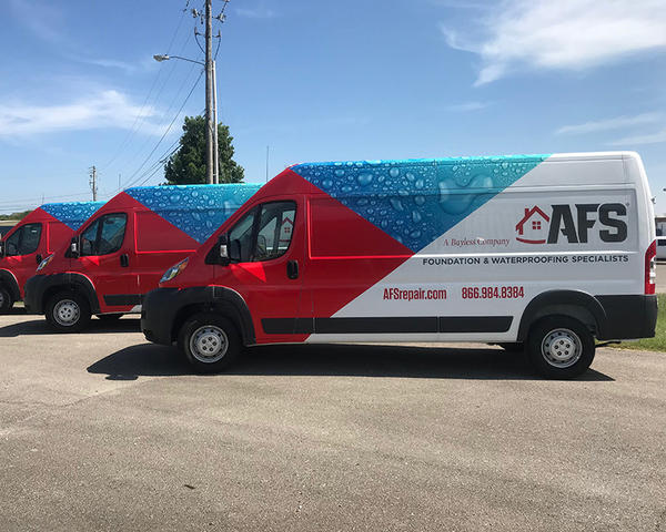 Three red and white AFS Foundation Specialists vans parked outdoors, adorned with water droplet designs and company details.