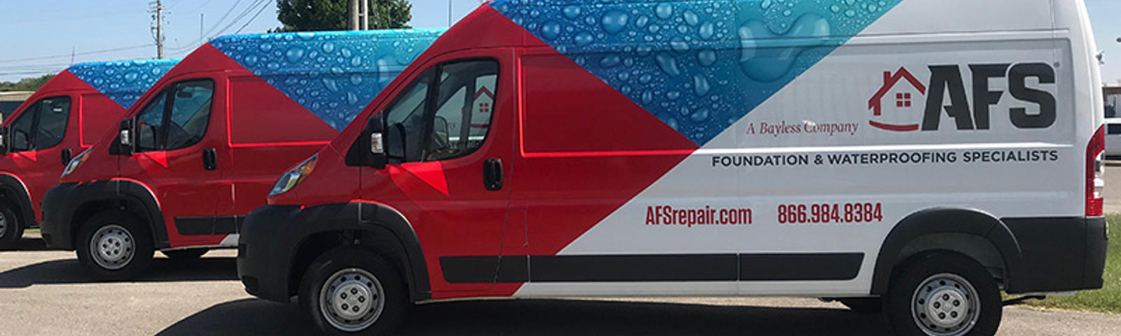 Three red and white AFS Foundation Specialists vans parked outdoors, adorned with water droplet designs and company details.