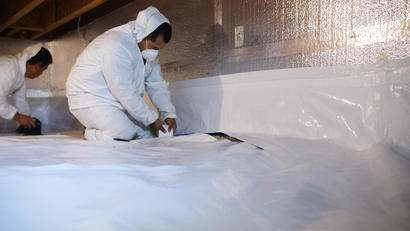 AFS crew member installing vapor barrier in crawl space.