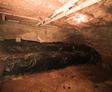 A dimly lit basement with exposed pipes, insulation, and a mound covered in plastic sheeting gives off typical crawl space smells.