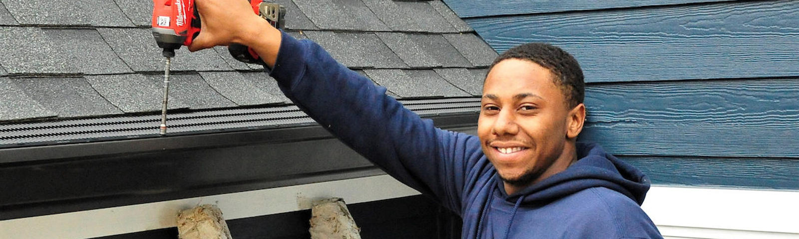 On a crisp Chattanooga morning, a person in a blue hoodie stands on a ladder, cheerfully using a drill to fix roof shingles.