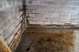 Damp basement corner with stained concrete floor and water-damaged cinder block walls, needing basement waterproofing.