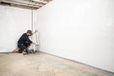 A worker installs white waterproof material on a basement wall—an essential step in basement waterproofing.