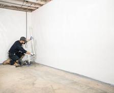 A worker installs white waterproof material on a basement wall—an essential step in basement waterproofing.