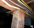 Rough wooden post supports a beam with notched wood; electrical wires run above—a reminder of reasons not to DIY foundation repair.
