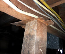 Rough wooden post supports a beam with notched wood; electrical wires run above—a reminder of reasons not to DIY foundation repair.