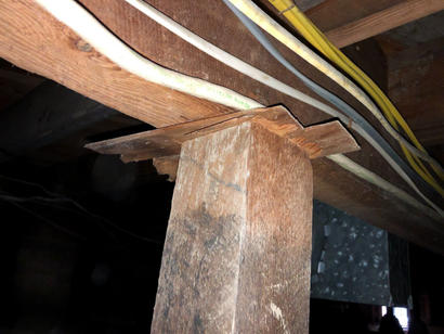 Rough wooden post supports a beam with notched wood; electrical wires run above—a reminder of reasons not to DIY foundation repair.