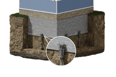 Cross-section of a house foundation with helical piers installed in the soil for stabilization support.