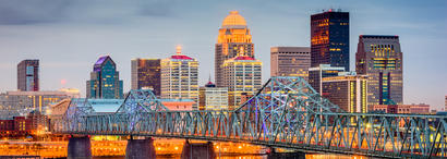 City skyline at dusk with illuminated buildings and a prominent bridge in the foreground.
