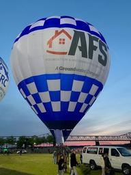 Hot air balloon with blue and white checkered pattern and logos, grounded near a van at dusk.