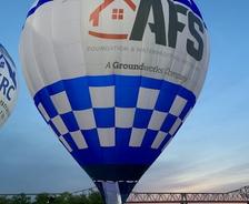 Hot air balloon with blue and white checkered pattern and logos, grounded near a van at dusk.