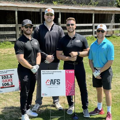 Four men in golf attire posing on a golf course next to a sponsorship sign.