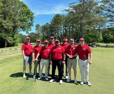 Eight men in matching red shirts and hats stand on a golf course, posing for a group photo.