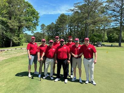 Eight men in matching red shirts and hats stand on a golf course, posing for a group photo.