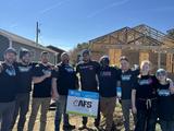 Group of volunteers smiling in front of a house under construction, holding a Habitat for Humanity sign.