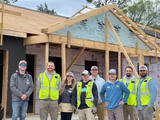 Group of construction workers in safety vests posing in front of a partially built house.