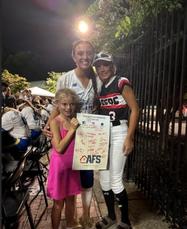 Three people smiling with a signed poster at an outdoor event.