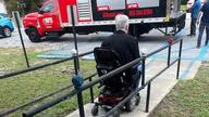 A person in a wheelchair using a ramp near a truck with red and white signage.