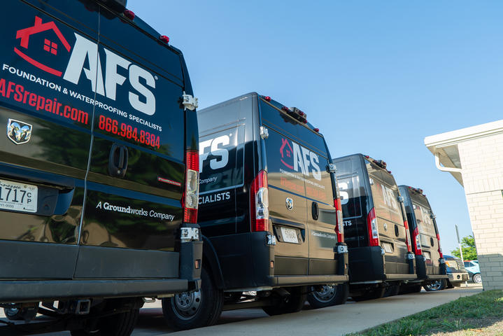 Four black AFS service vans, glowing under the sunny day, parked in a row near a building, garner positive reviews from passersby.