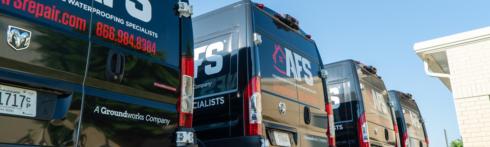 Four black AFS service vans, glowing under the sunny day, parked in a row near a building, garner positive reviews from passersby.